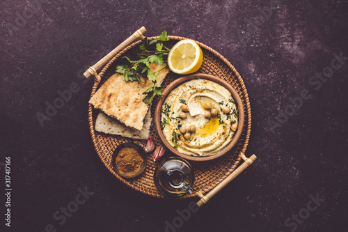 Large bowl of homemade hummus garnished with chickpeas, red sweet pepper, parsley and olive oil