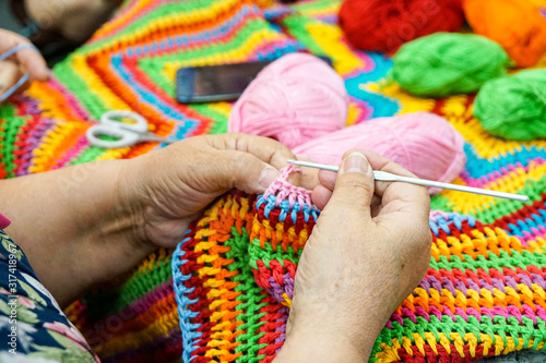 hands of an old woman with knitting needles, knitting from multi-colored yarn