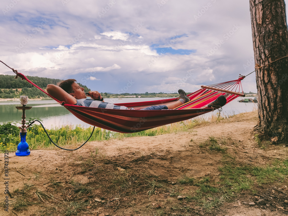 man laying at hammock smoking hookah looking at lake beach