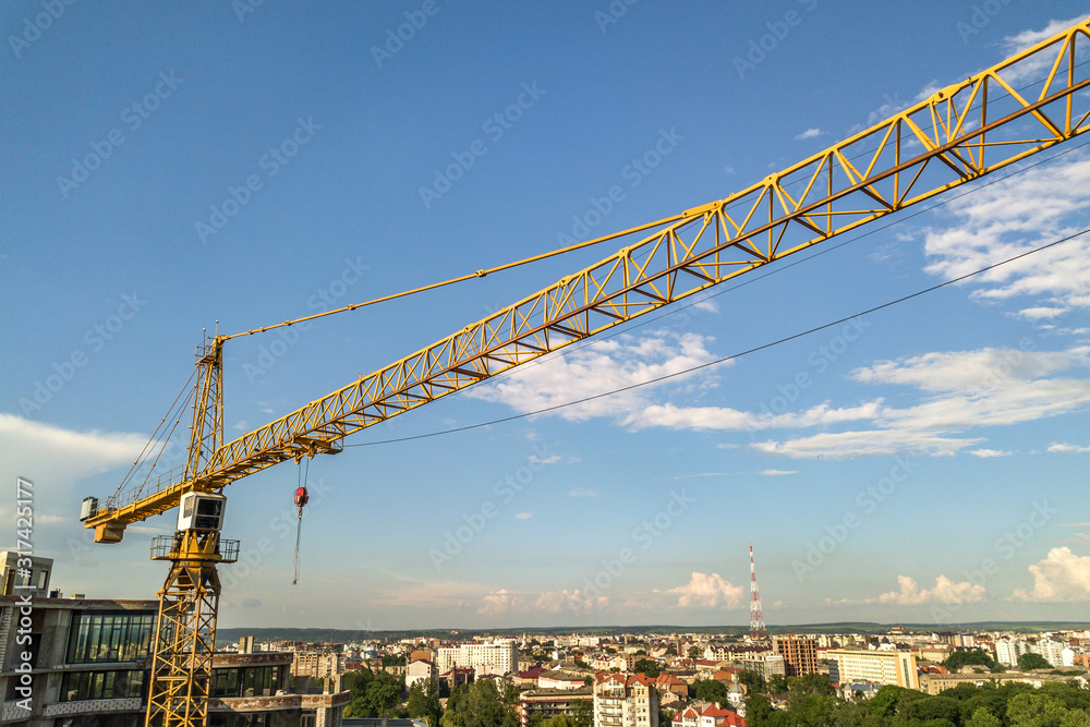 Apartment or office tall building under construction. Brick walls, glass windows, scaffolding and concrete support pillars. Tower crane on bright blue sky copy space background. Apartment or office tall building under construction. Brick walls, glass windows, scaffolding and concrete support pillars. Tower crane on bright blue sky copy space background.