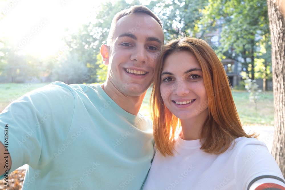 Obraz premium Happy young couple taking selfie outdoors in warm sunny weather.
