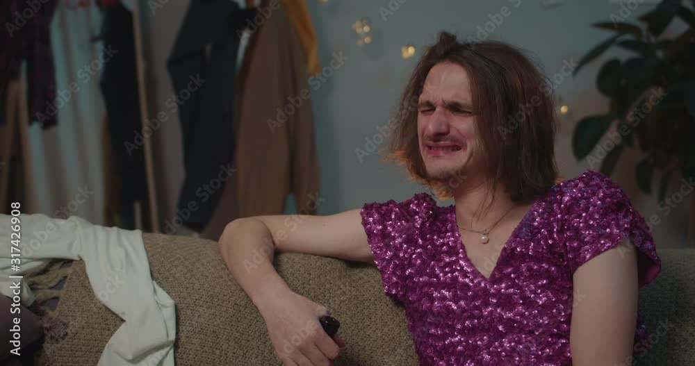 Close up of upset drunk transgender man sitting on sofa with wine bottle. Man trans feeling lonely after breakup, holding wine and crying. Concept of people and emotions. Home background. Close up of upset drunk transgender man sitting on sofa with wine bottle. Man trans feeling lonely after breakup, holding wine and crying. Concept of people and emotions. Home background.