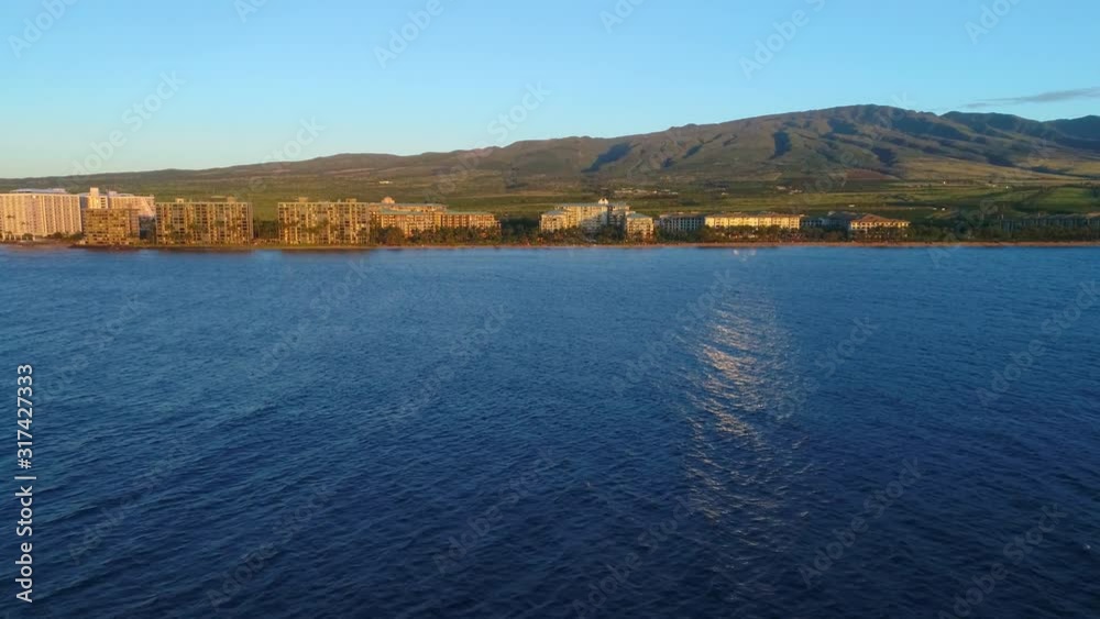 Stunning seascape with glowing resort buildings on shore of Hawaiian island seen from deep blue sea at sunset Stunning seascape with glowing resort buildings on shore of Hawaiian island seen from deep blue sea at sunset