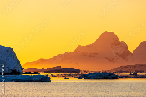 Golden yellow sunset over the mountains, water, and icebergs of Antarctica, a pristine remote landscape