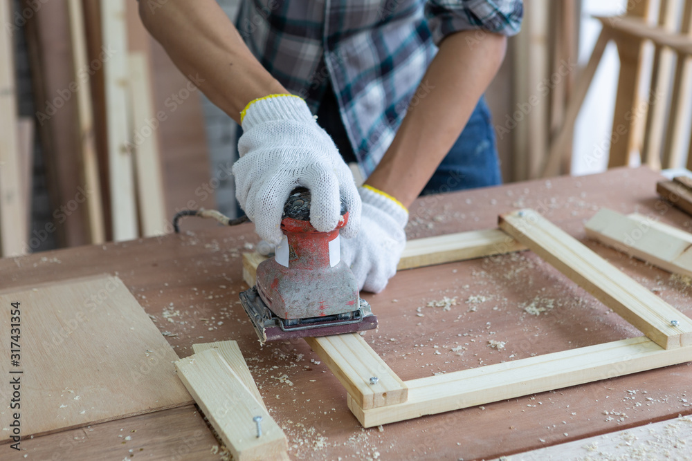 Closeup young asian carpenter polishing wooden job with sanding machine - Handyman and diy concept