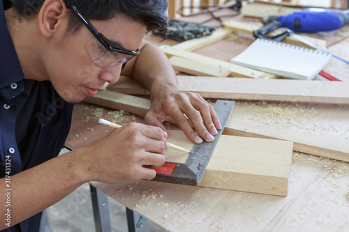 Closeup hands of young asian carpenter measuring on wooden job with try square - Handyman and diy concept photo