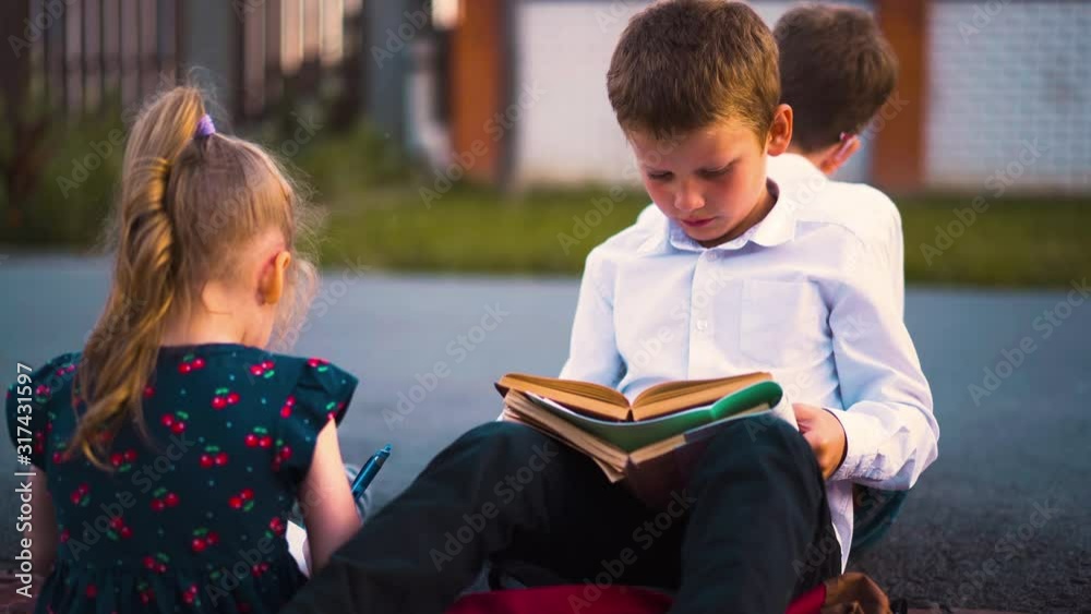 funny little girl with ponytail holds blue pencil talks to student reading textbook with friend in sunny street close funny little girl with ponytail holds blue pencil talks to student reading textbook with friend in sunny street close