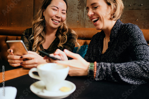 Two female friends in a cafe having coffee, smiling and chatting	