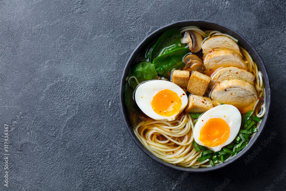 Asian noodle soup, ramen with chicken, tofu, vegetables and egg in black bowl. Slate background. Copy space. Top view. Asian noodle soup, ramen with chicken, tofu, vegetables and egg in black bowl. Slate background. Copy space. Top view.