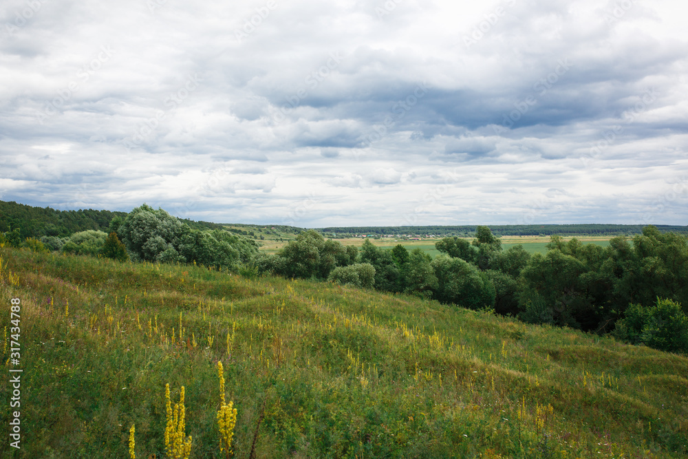 Path in a green field, panoramic view of the river in summer. View from the top of the hill
