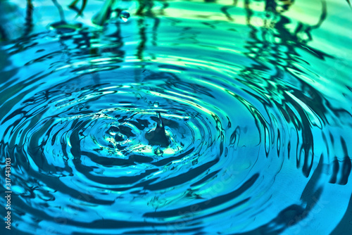 Raindrops fall on the surface of the water. The circles from the raindrops on the water surface. Abstract color background of circles on the water and falling drops.