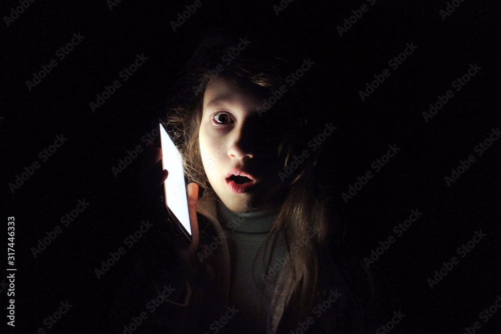 Child girl with a phone in the dark. Frightened child calls to mother: power outage. Child girl with a phone in the dark. Frightened child calls to mother: power outage.