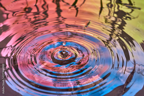 Raindrops fall on the surface of the water. The circles from the raindrops on the water surface. Abstract color background of circles on the water and falling drops.
