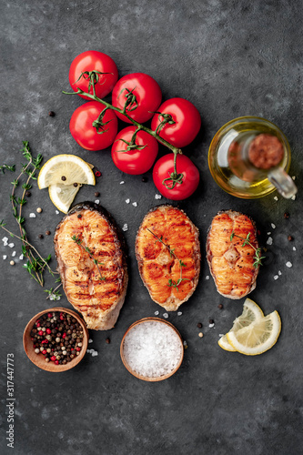 Three grilled salmon steaks with spices, lemon and tomatoes on a stone background