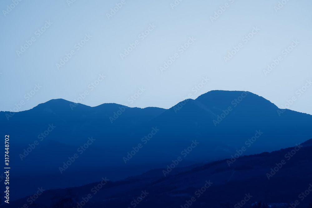 Scenic views of mountain landscape, rocks and valley in summer toned in trendy Classic Blue color of the Year 2020.  Beautiful minimalist landscape of mountain ranges covered with forest.