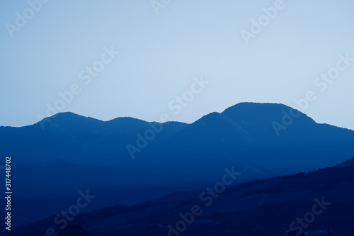 Scenic views of mountain landscape, rocks and valley in summer toned in trendy Classic Blue color of the Year 2020. Beautiful minimalist landscape of mountain ranges covered with forest.