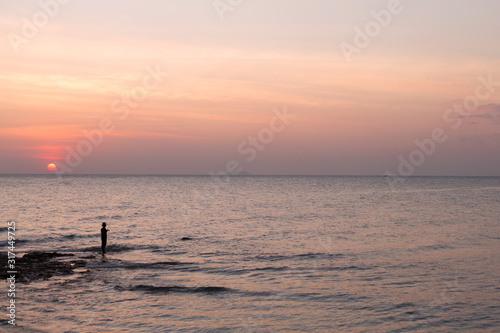 Fisherman in the hat on sea pink sunset background.
