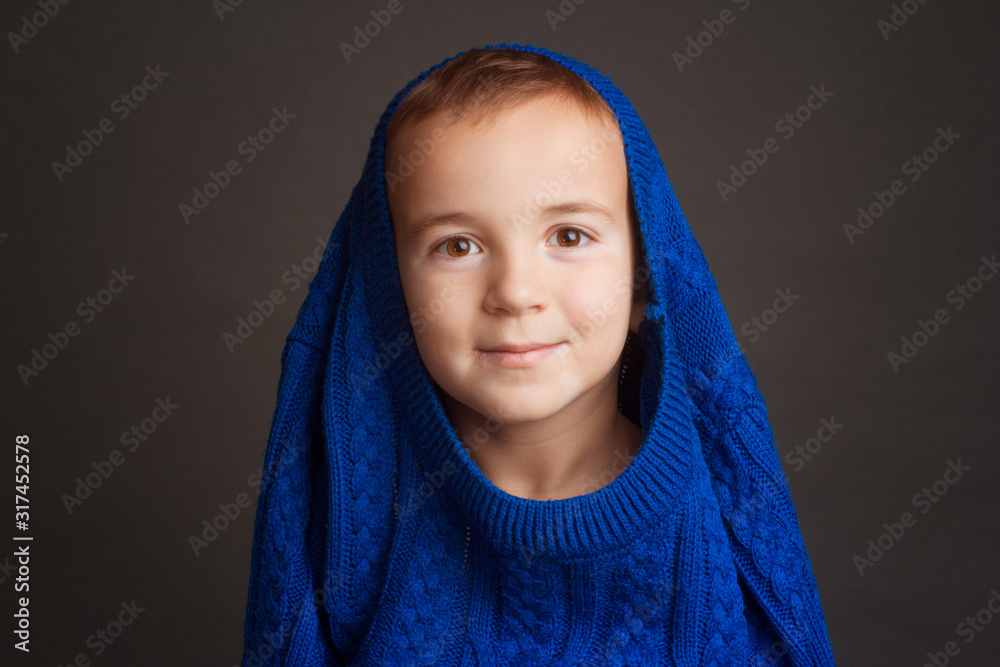 Studio portrait of dark-haired boy with short haircut in a blue classic knitted sweater pulled playfully over his head. The concept of play, pampering and joy. Studio portrait of dark-haired boy with short haircut in a blue classic knitted sweater pulled playfully over his head. The concept of play, pampering and joy.