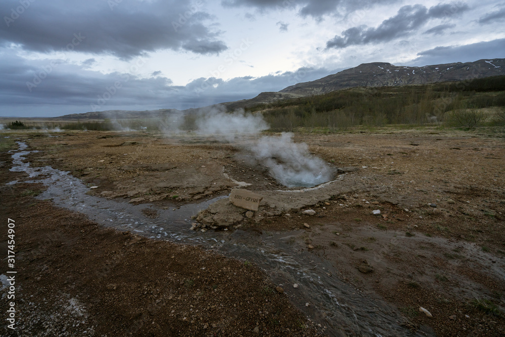 Litli-geysir or mini geysir next to Strokkur in Haukaalur area in the Icelandic countryside. Blue hour and cloudy sky with boiling hot pool infront. Travelin concept.