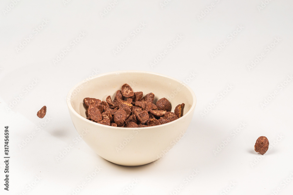 Chocolate corn flakes falling to the white bowl isolated on white. Motion. Chocolate corn flakes falling to the white bowl isolated on white. Motion.