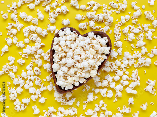 Top view on a wooden bowl in the form of a heart with popcorn