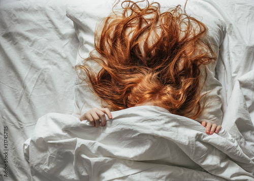 Red-haired little girl wakes up in the morning in her crib