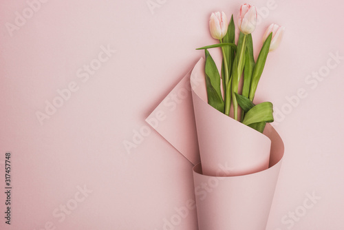 top view of tulips wrapped in paper on pink background
