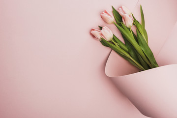 Top view of tulip bouquet wrapped in paper swirl on pink background