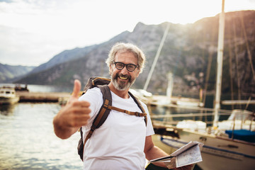 Smiling tourist mature man standing with map and backpack near the sea.