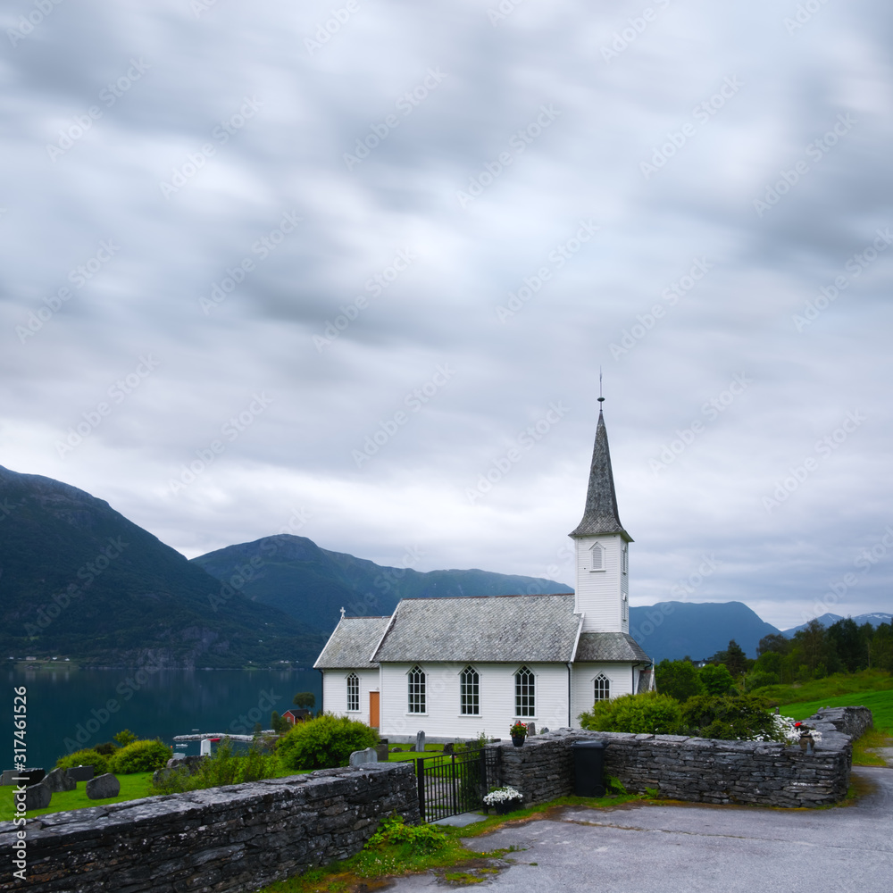Typical christianity church with cemetery of Nes village, parish church in Luster Municipality in Sogn og Fjordane county, Norway. Lustrafjorden fjord on background. Landscape photography