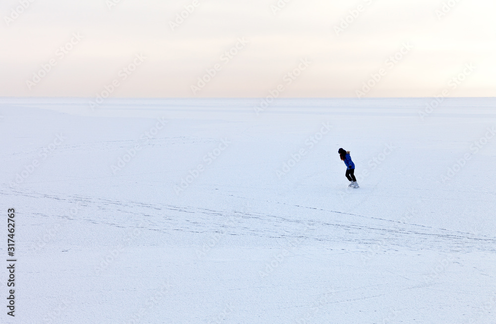 Frozen Lake Baikal in January. Endless white desert of snowy ice. Lonely girl tourist skates on ice on a frosty morning at dawn. Winter landscape. Natural background Frozen Lake Baikal in January. Endless white desert of snowy ice. Lonely girl tourist skates on ice on a frosty morning at dawn. Winter landscape. Natural background