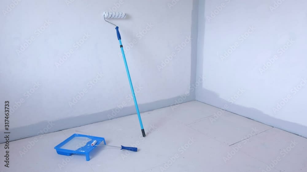 Two paint rollers and paint pan with grey paint in room near wall