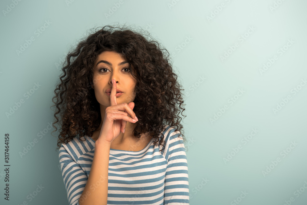 pretty mixed race girl showing hush gesture while looking at camera on grey background pretty mixed race girl showing hush gesture while looking at camera on grey background