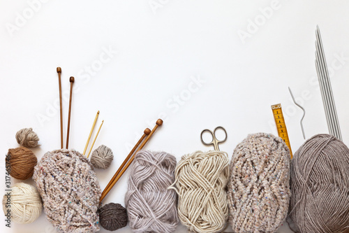 Accessories for hand knitting and balls of woolen yarn in beige colors on a white background. Hand knitting and needlework concept. Free space for text, flat lay, close-up, copy space, top view