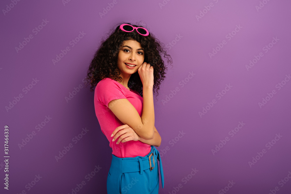 attractive bi-racial girl smiling at camera while holding hand near face on purple background attractive bi-racial girl smiling at camera while holding hand near face on purple background