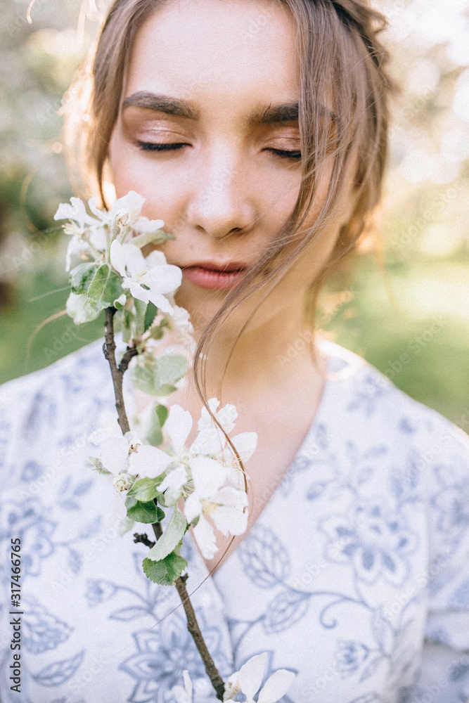 Fototapeta premium Portrait of young beautiful girl in white lace dress in apple garden, in the tree crown, fingers near mouth