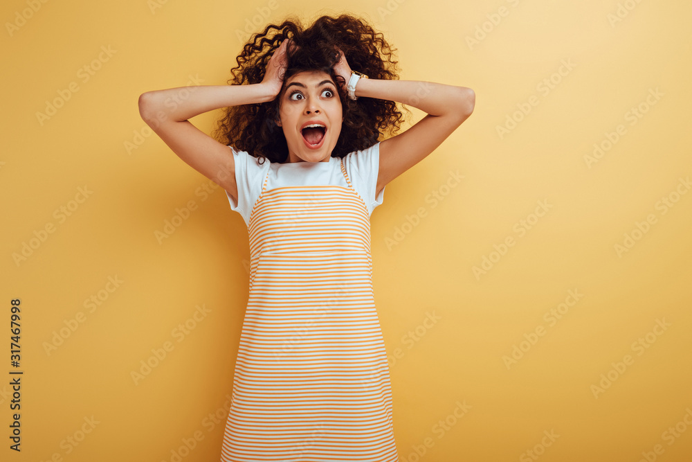 shocked mixed race girl touching head and looking away on yellow background shocked mixed race girl touching head and looking away on yellow background