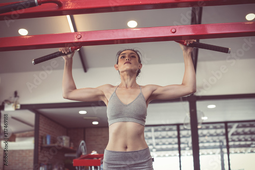 female adults doing pull ups on bar in cross fit training gym. photo of muscular woman in sportswear. fitness women exercising are lifting bar at vintage fitness gym. concept strength and motivation.