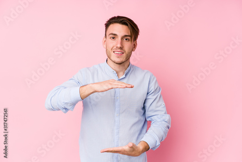 Young caucasian man posing in a pink background isolated holding something with both hands, product presentation.