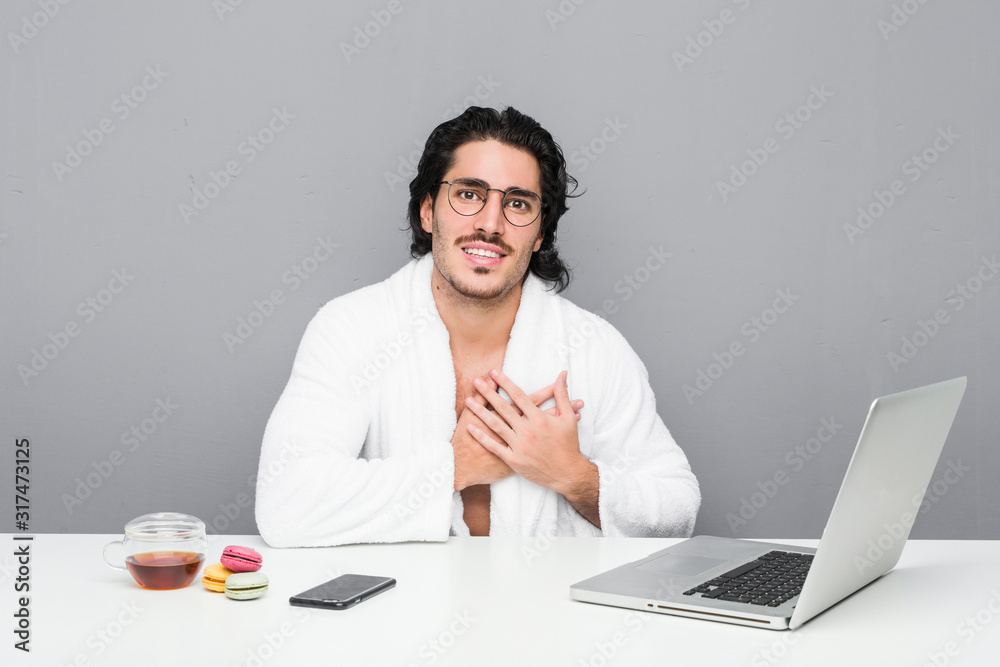 Young handsome man working after a shower has friendly expression, pressing palm to chest. Love concept. Young handsome man working after a shower has friendly expression, pressing palm to chest. Love concept.