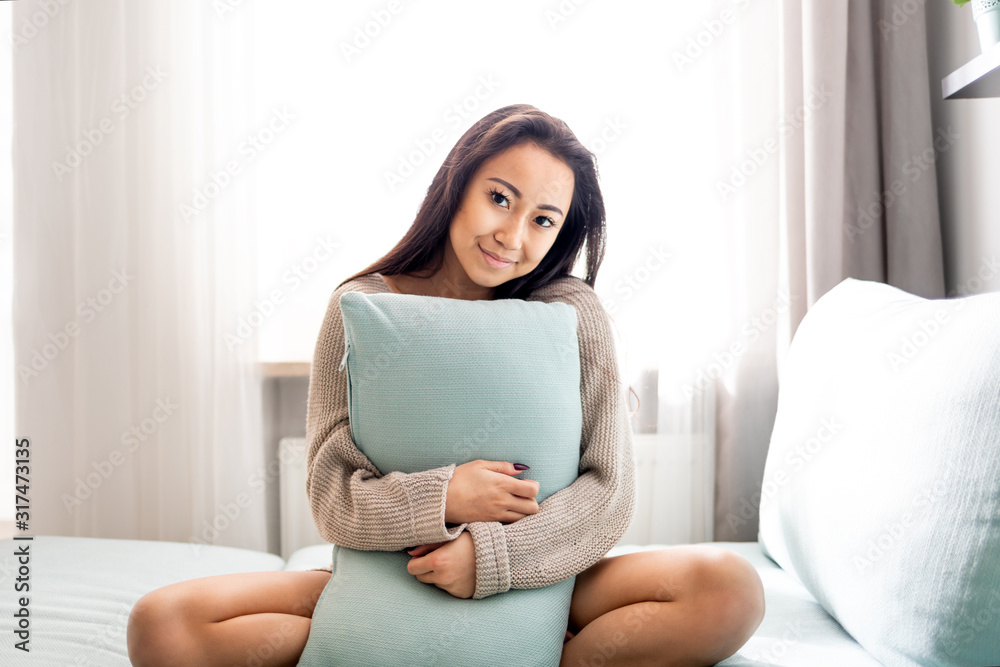 Cute asian young woman sitting on sofa with pillow at home