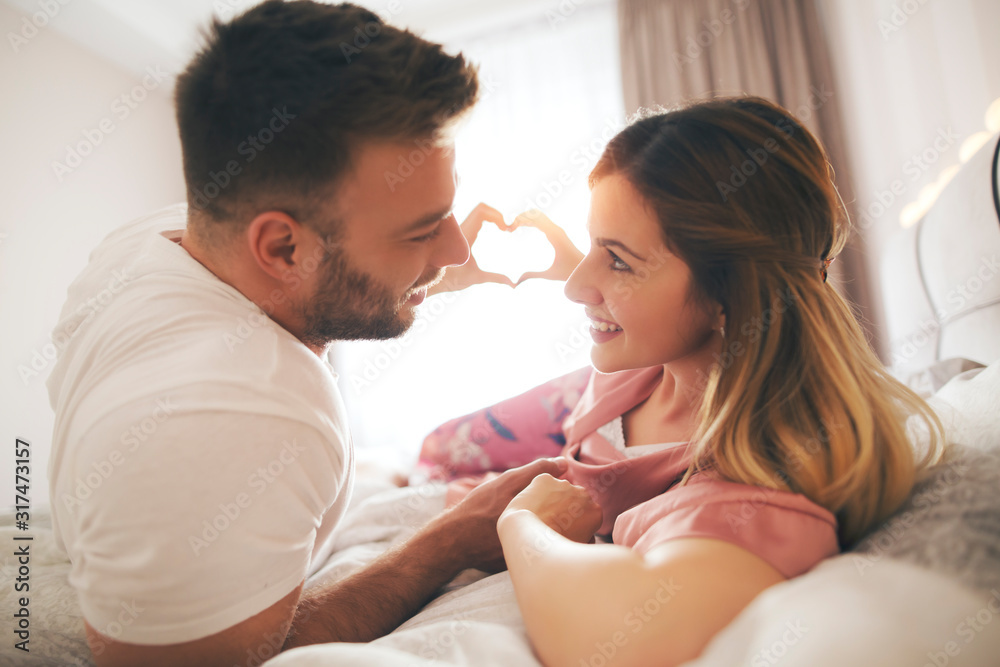 Beautiful couple in bed showing heart symbol with their hands. Beautiful couple in bed showing heart symbol with their hands.