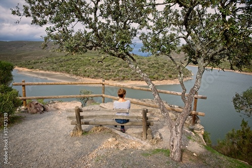 Obraz na plátně A woman sitting on a bench contemplates a river meander