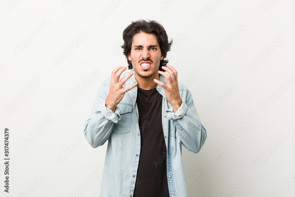 Young handsome man against a white background upset screaming with tense hands. Young handsome man against a white background upset screaming with tense hands.