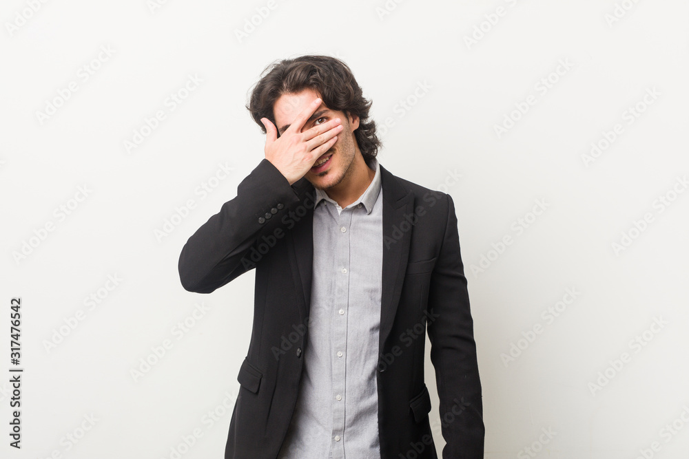 Young business man against a white background blink at the camera through fingers, embarrassed covering face. Young business man against a white background blink at the camera through fingers, embarrassed covering face.