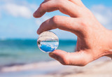 Close-up on Person's Hand Holding Mini Glass Ball and Beach Background