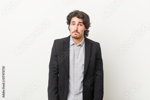 Young business man against a white background shrugs shoulders and open eyes confused.