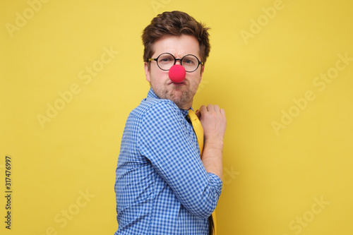 Fotografija A young greedy man with red clown nose hides something in his hands and looks wa