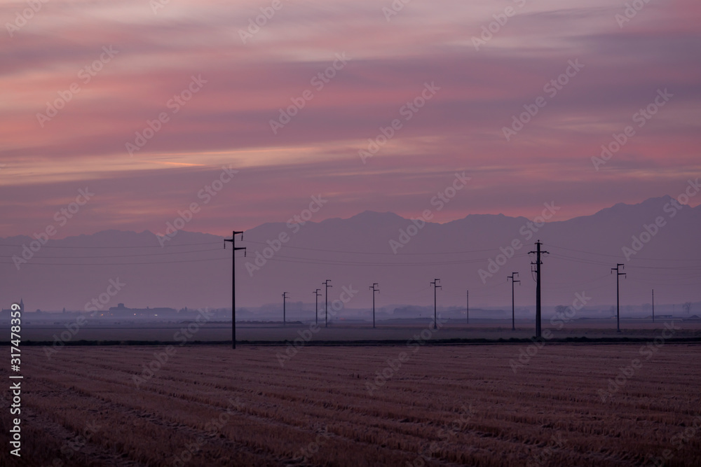 Obraz premium Sunset landscape in the countryside with power line, poles and old farms in the Piedmont plain, Po valley, Italy