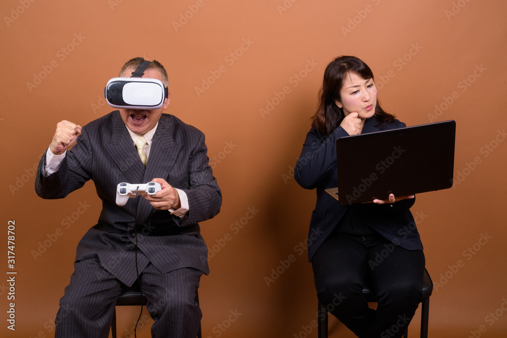 Obraz premium Mature Asian businesswoman with mature Asian businessman playing games